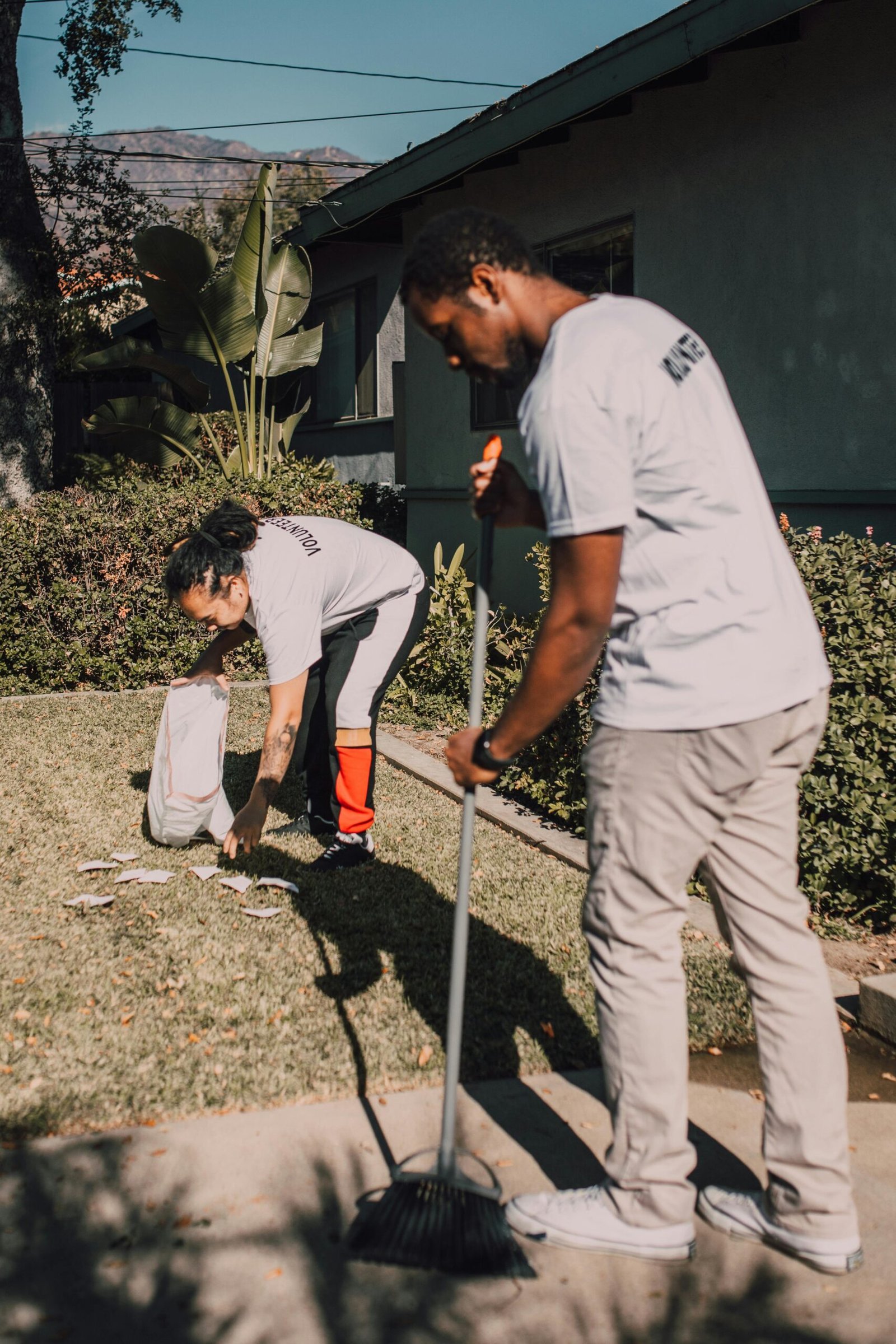 Two volunteers working together to clean a garden with a rake and collecting bags.